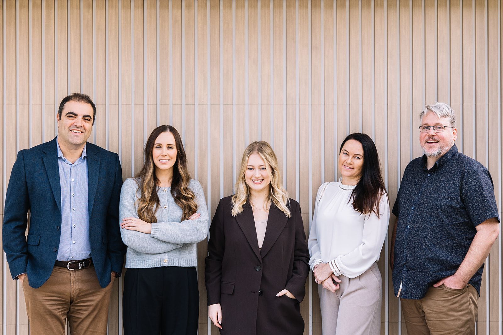 Group of Five Professionals Standing in Front of A Beige Wall — The Garis Group  In Hamilton, NSW