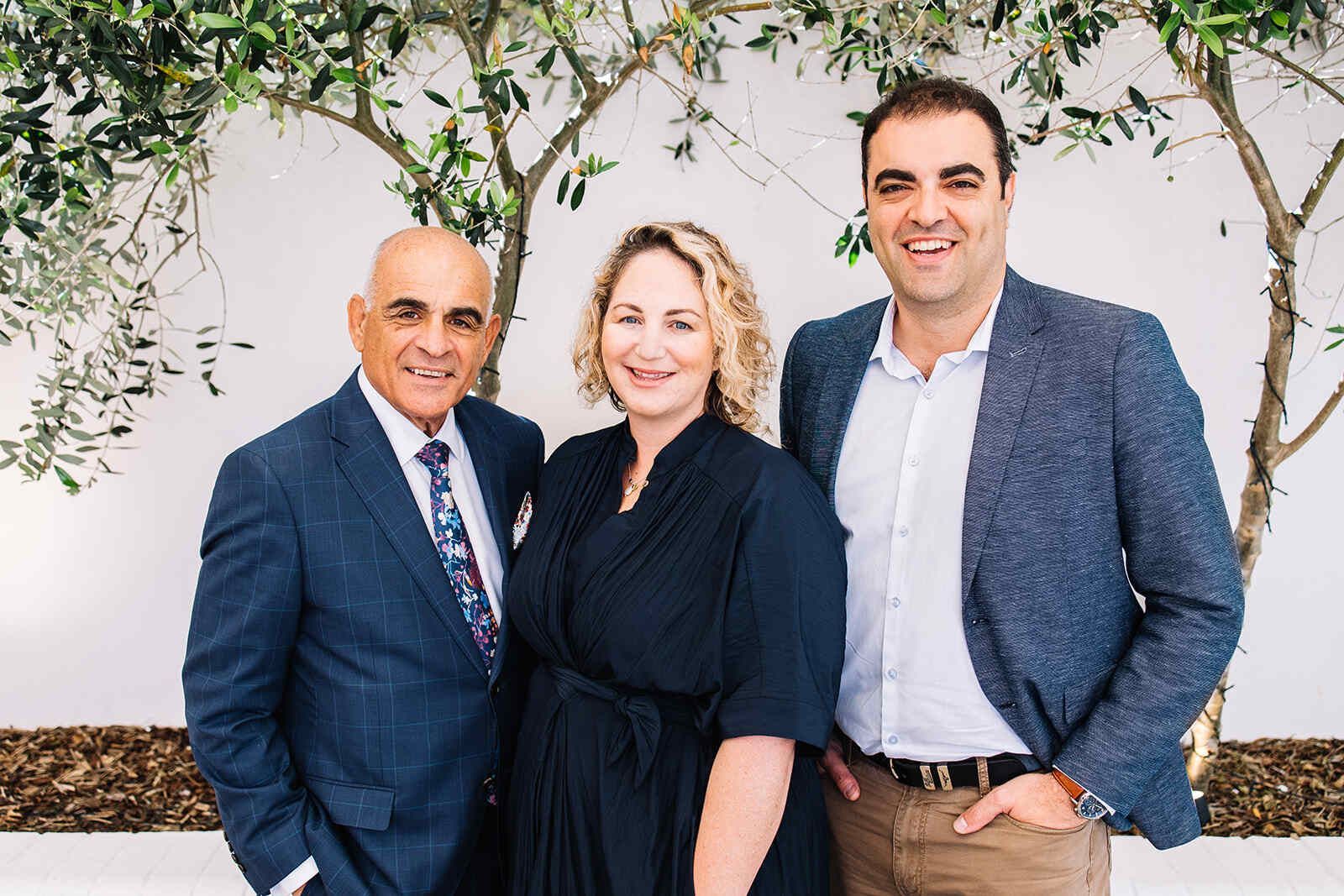 A Group Of Three People Standing Next To Each Other In Front Of A Tree — The Garis Group In Hamilton, NSW