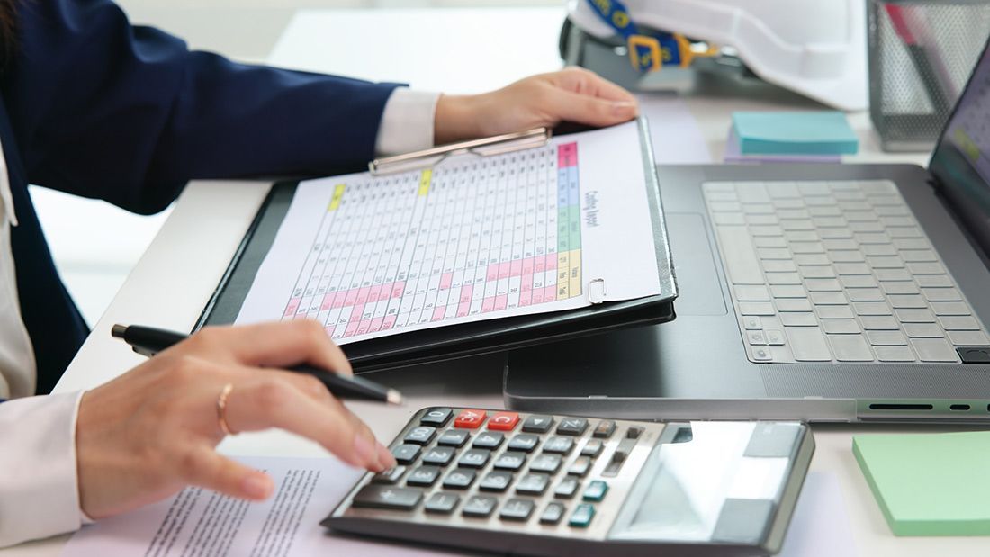 A Woman is Sitting at a Desk Using a Calculator and a Laptop — The Garis Group in Hamilton, NSW