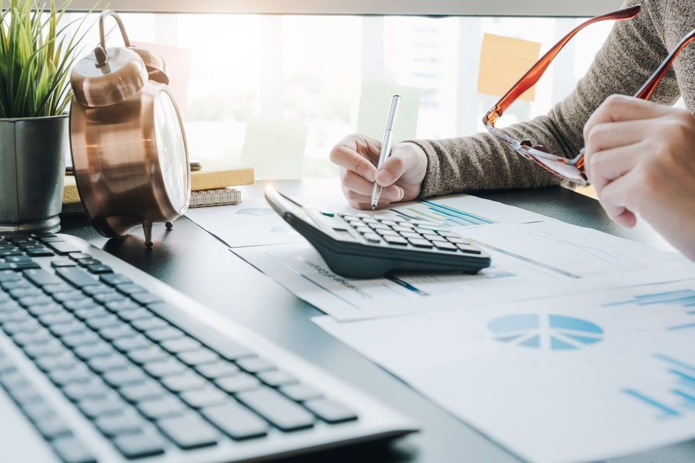 A Person Is Sitting At A Desk With A Calculator And A Pen — The Garis Group  In Hamilton, NSW 