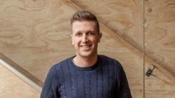 A Man In A Blue Sweater Is Standing In Front Of A Wooden Wall — The Garis Group  In Hamilton, NSW 