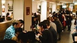 A Group Of People Are Sitting At Tables In A Restaurant — The Garis Group  In Hamilton, NSW