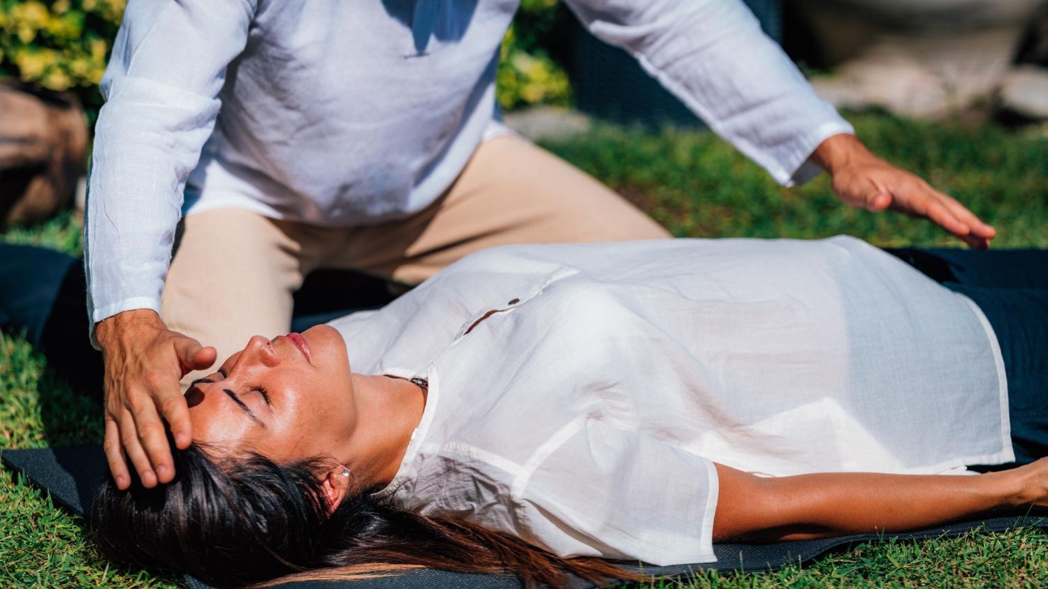 Person receiving energy healing outdoors; practitioner with hands on her head.