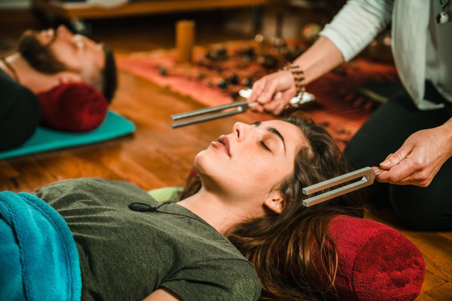 Person receiving a sound healing treatment with tuning forks, lying on a mat in a warm room