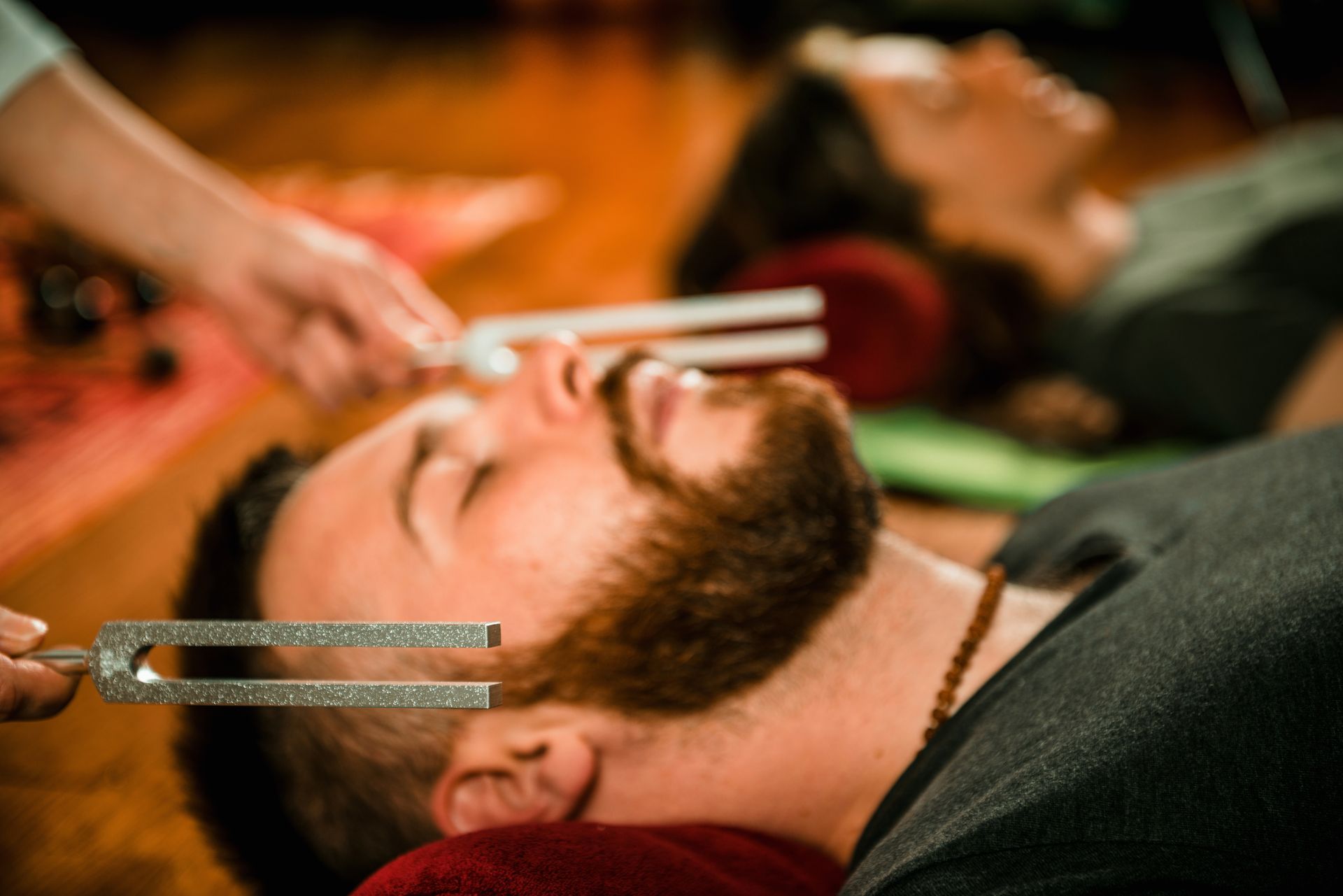 Two people receiving sound healing, lying down with tuning forks near their faces.
