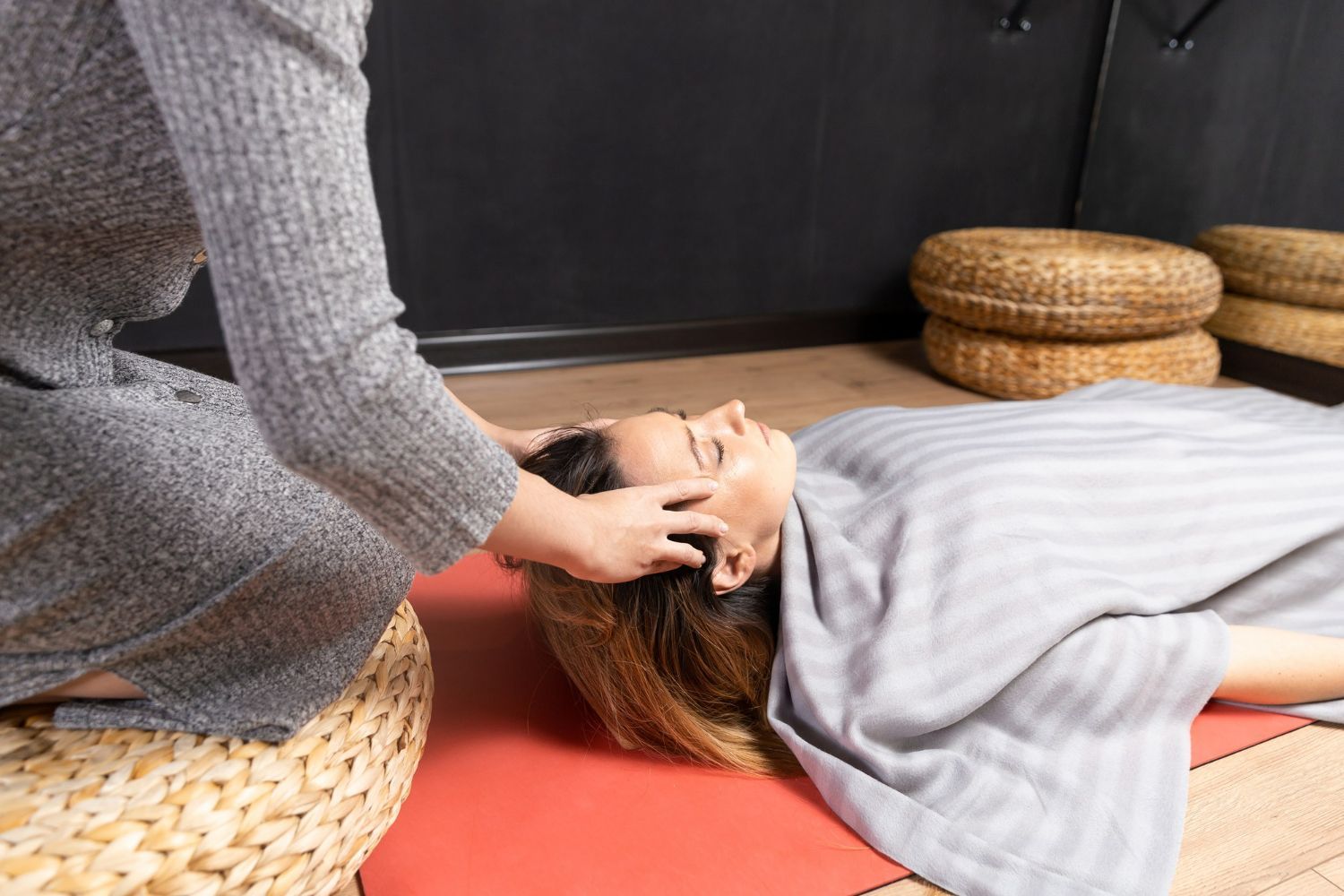 A woman is laying on a yoga mat getting a head massage.