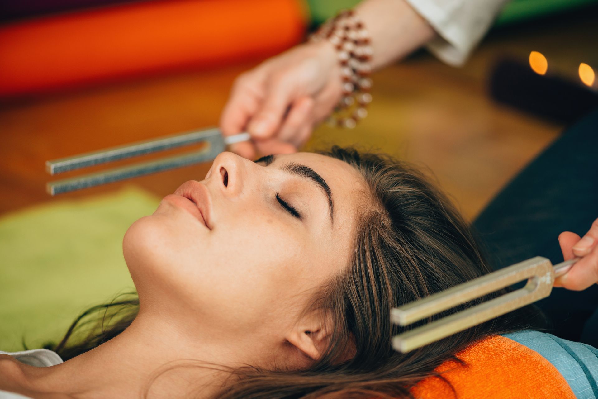 Woman receiving sound therapy with tuning forks held near her head, eyes closed.