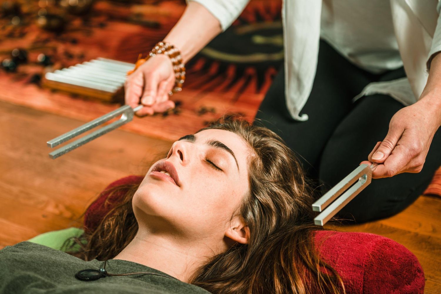 A woman is laying on the floor getting a massage with a tuning fork.