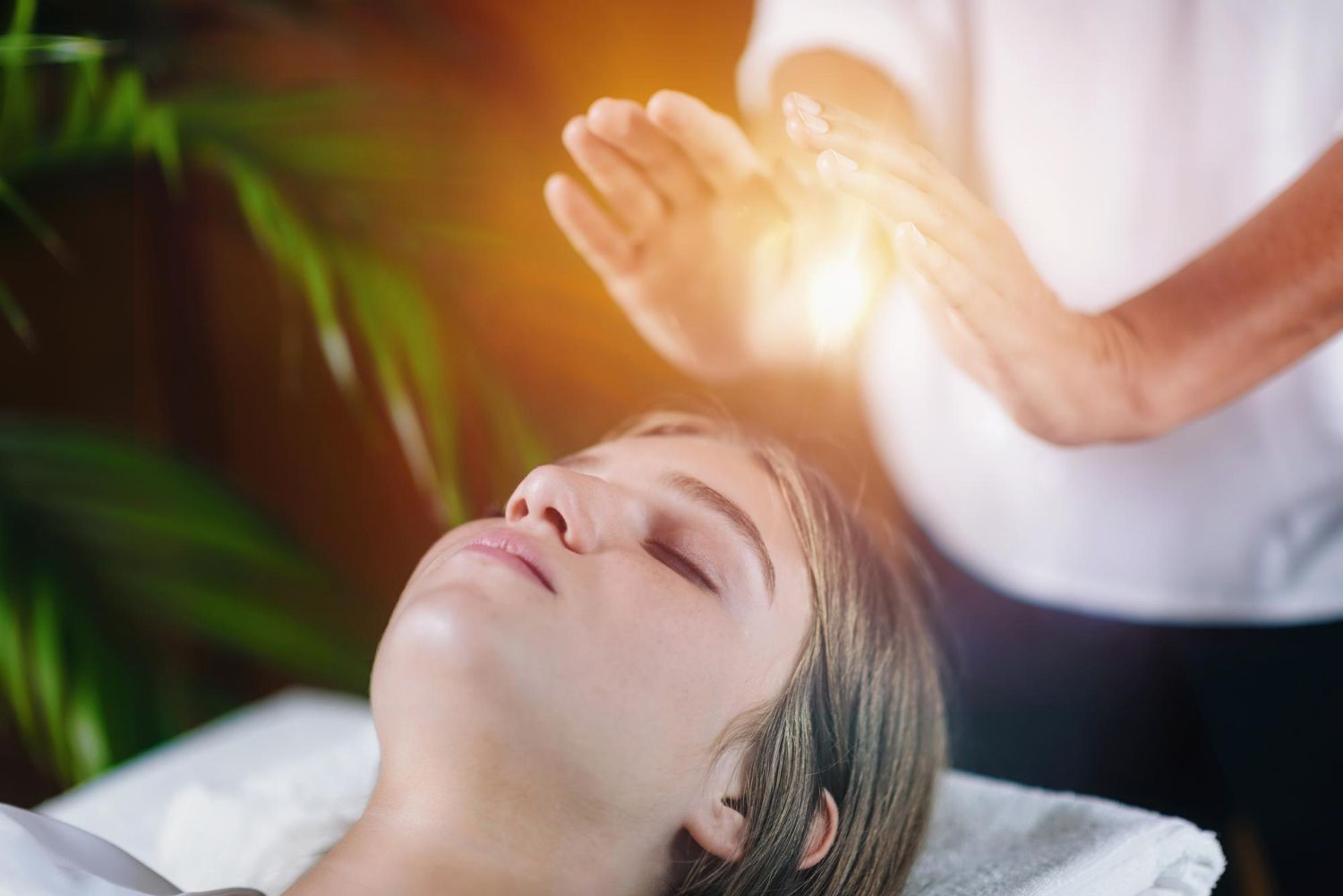 Woman receiving energy healing; hands glowing near her head, eyes closed.