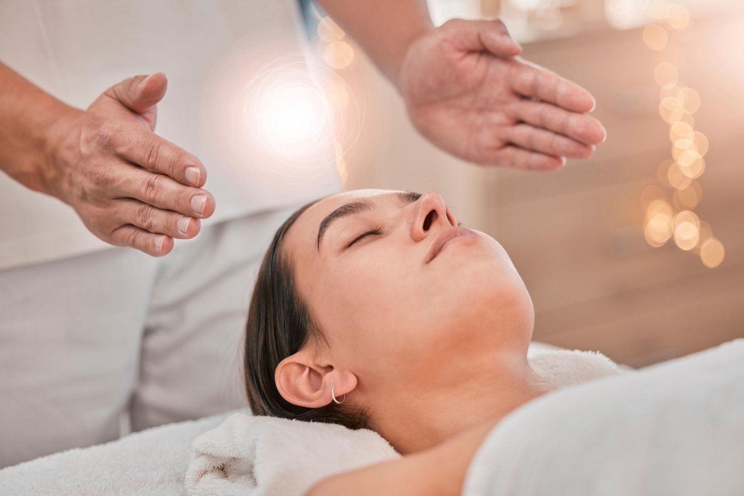 Hands hovering over a woman lying on a spa bed during a facial treatment