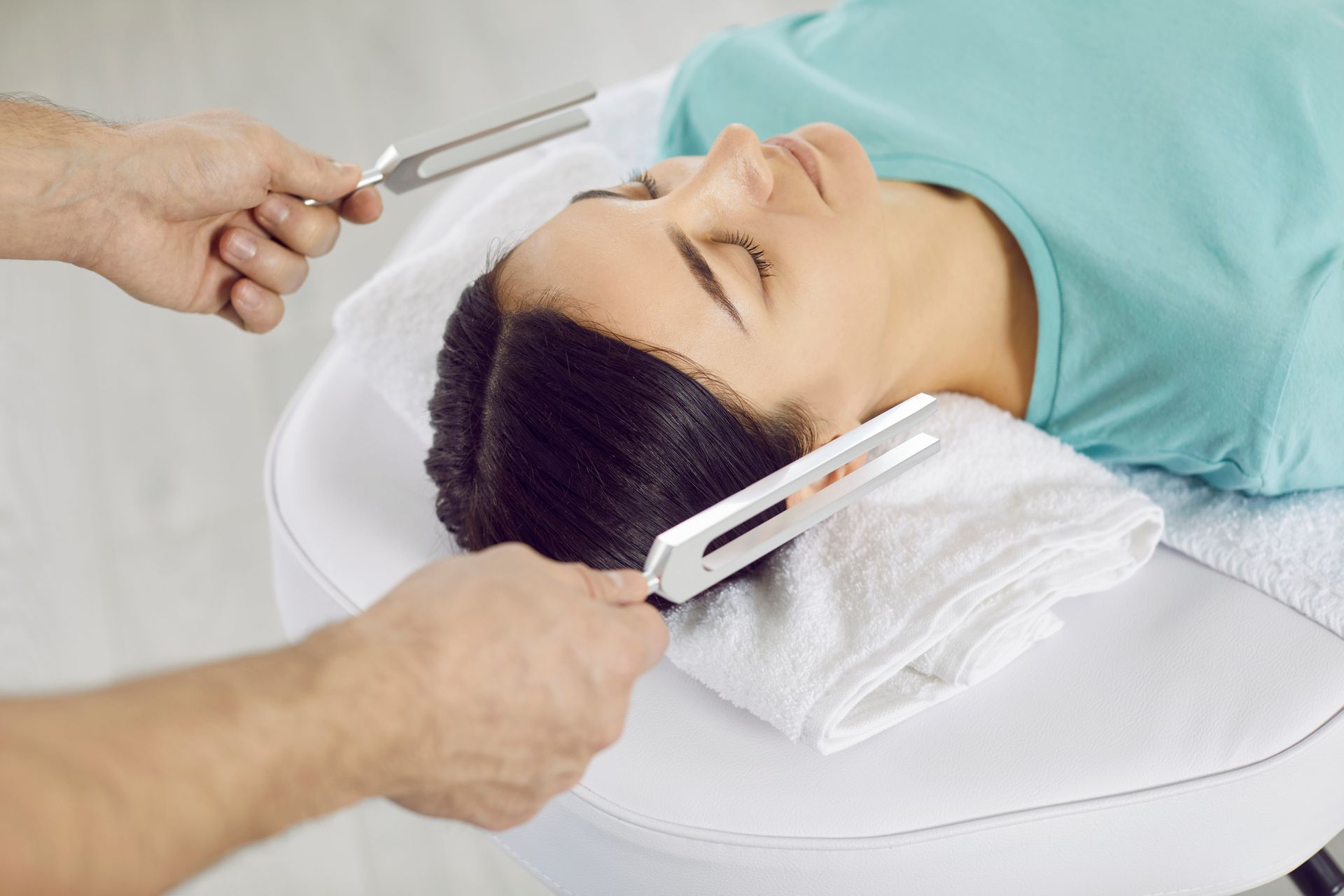 Person receiving sound healing with tuning forks held near head.