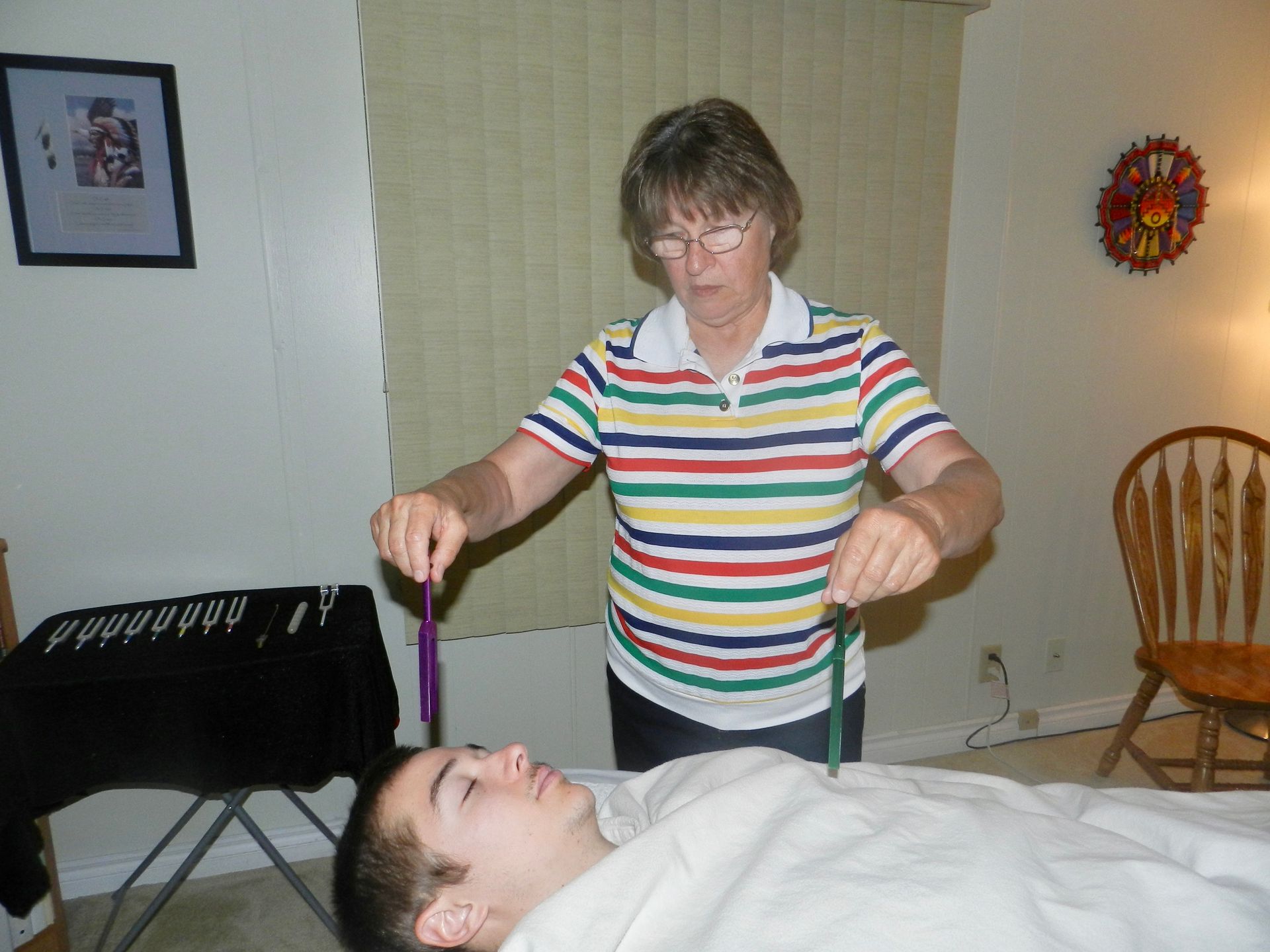 A woman in a striped shirt is holding a purple wand over a man laying on a bed