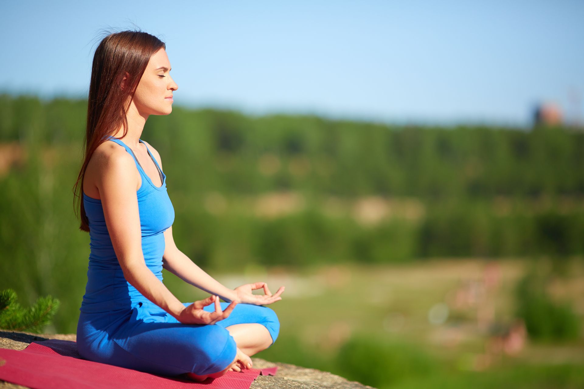 Woman in blue yoga attire meditating outdoors with eyes closed.