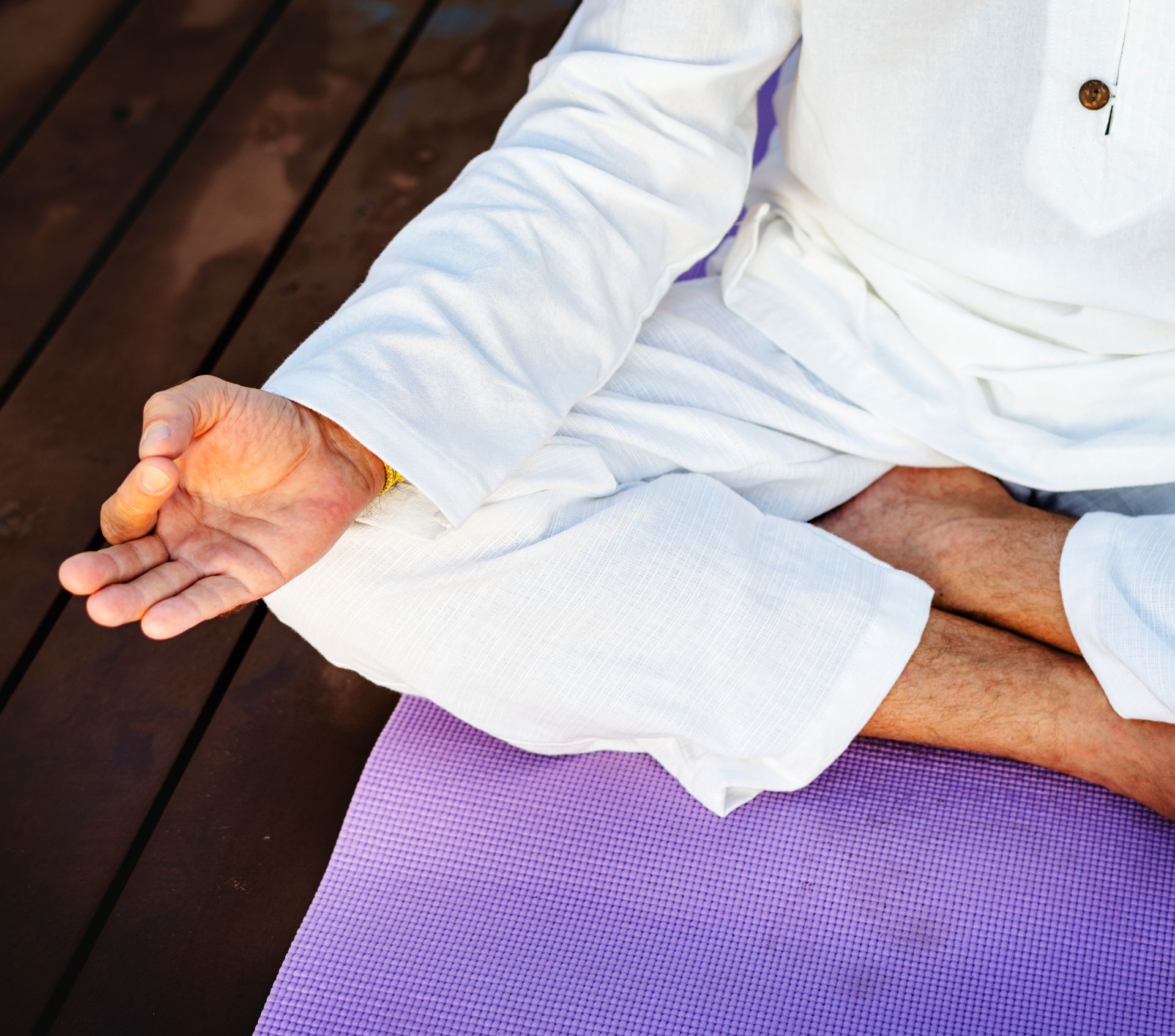 Person in white clothing meditating on a purple mat.