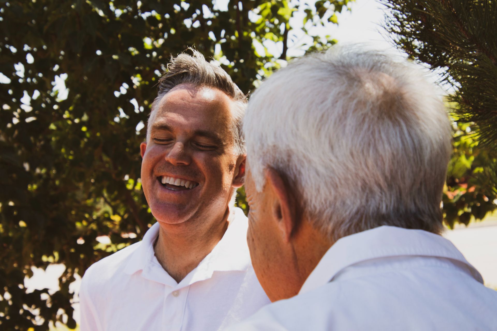 two men in white shirts are laughing with their eyes closed
