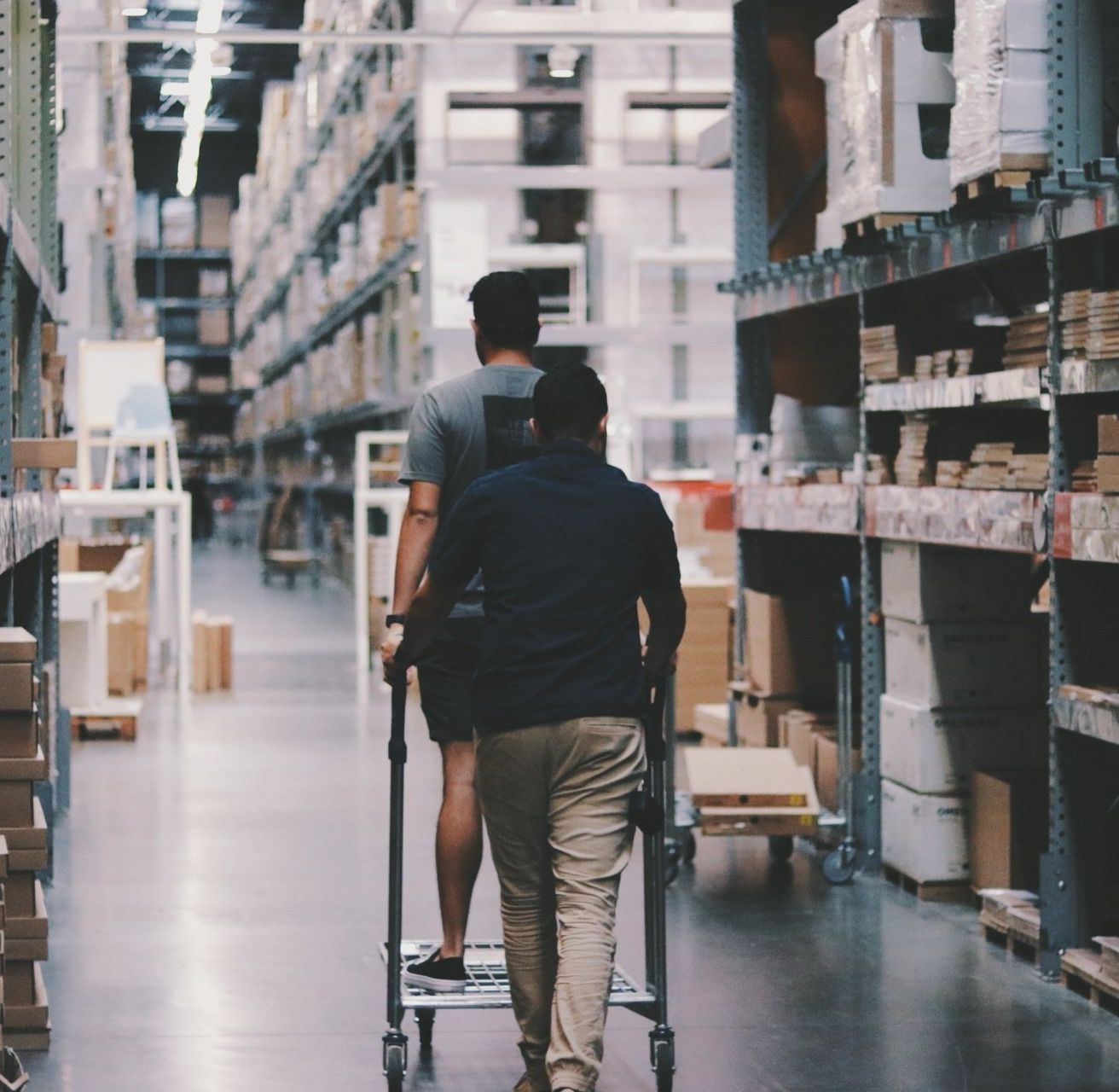 two men pushing a cart in a warehouse with boxes on the shelves