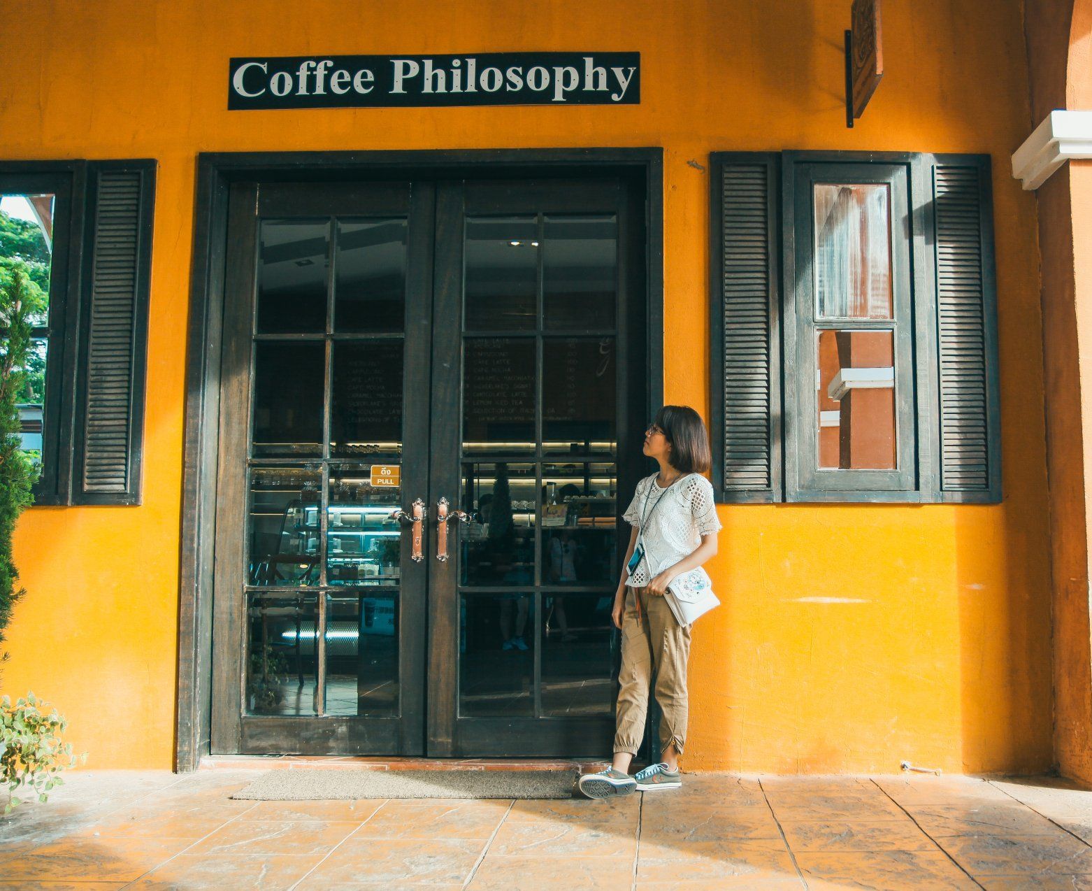 a woman stands in front of a coffee philosophy store