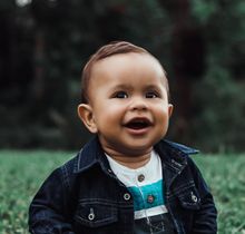 a baby wearing a denim jacket and striped shirt is smiling