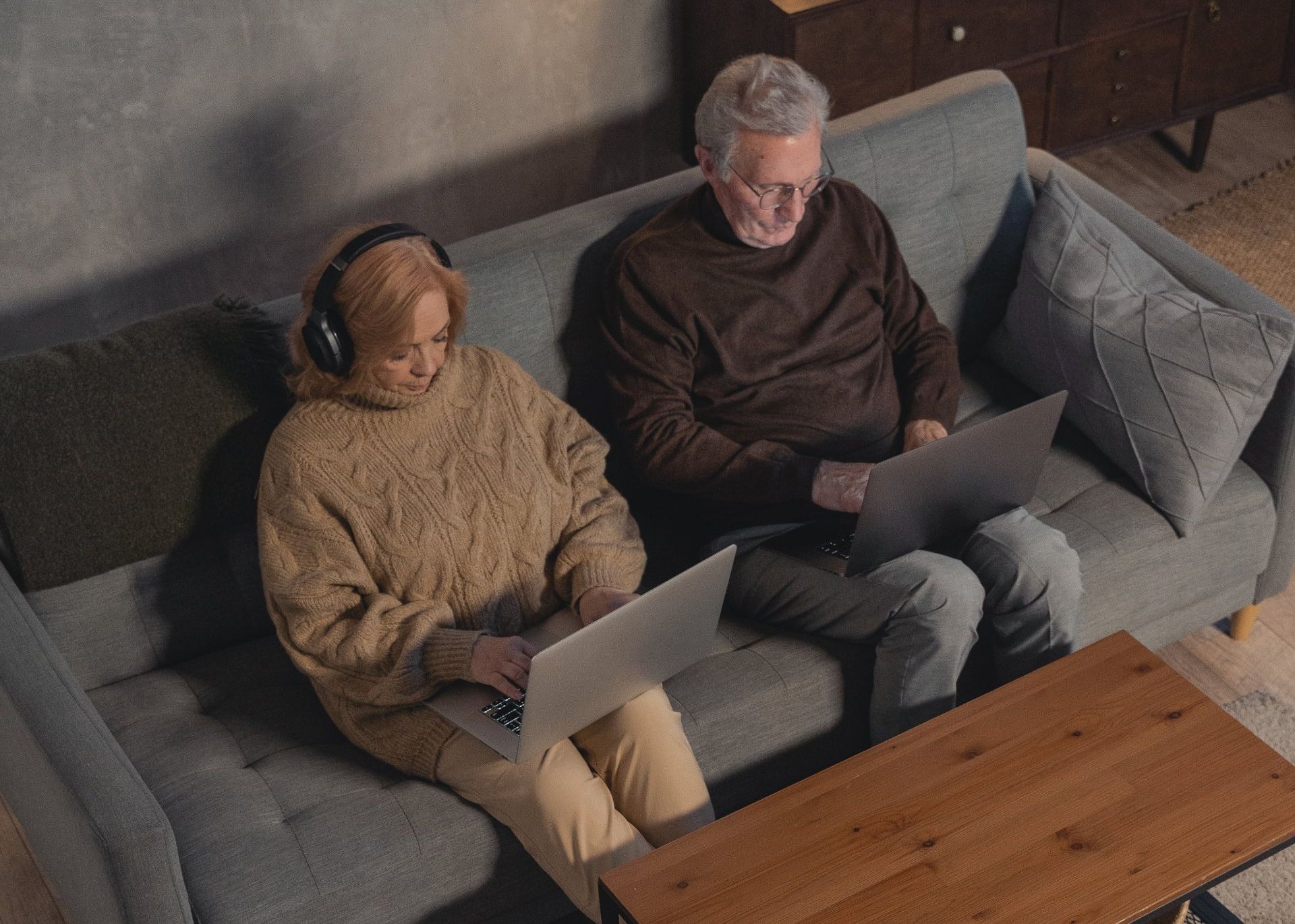 a man and a woman sit on a couch using laptops