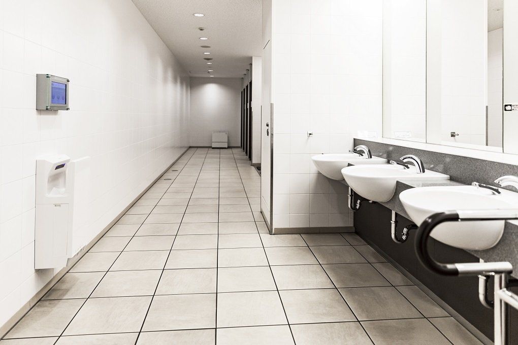 Long hallway of a public restroom with sinks on the right and a hand dryer on the left.