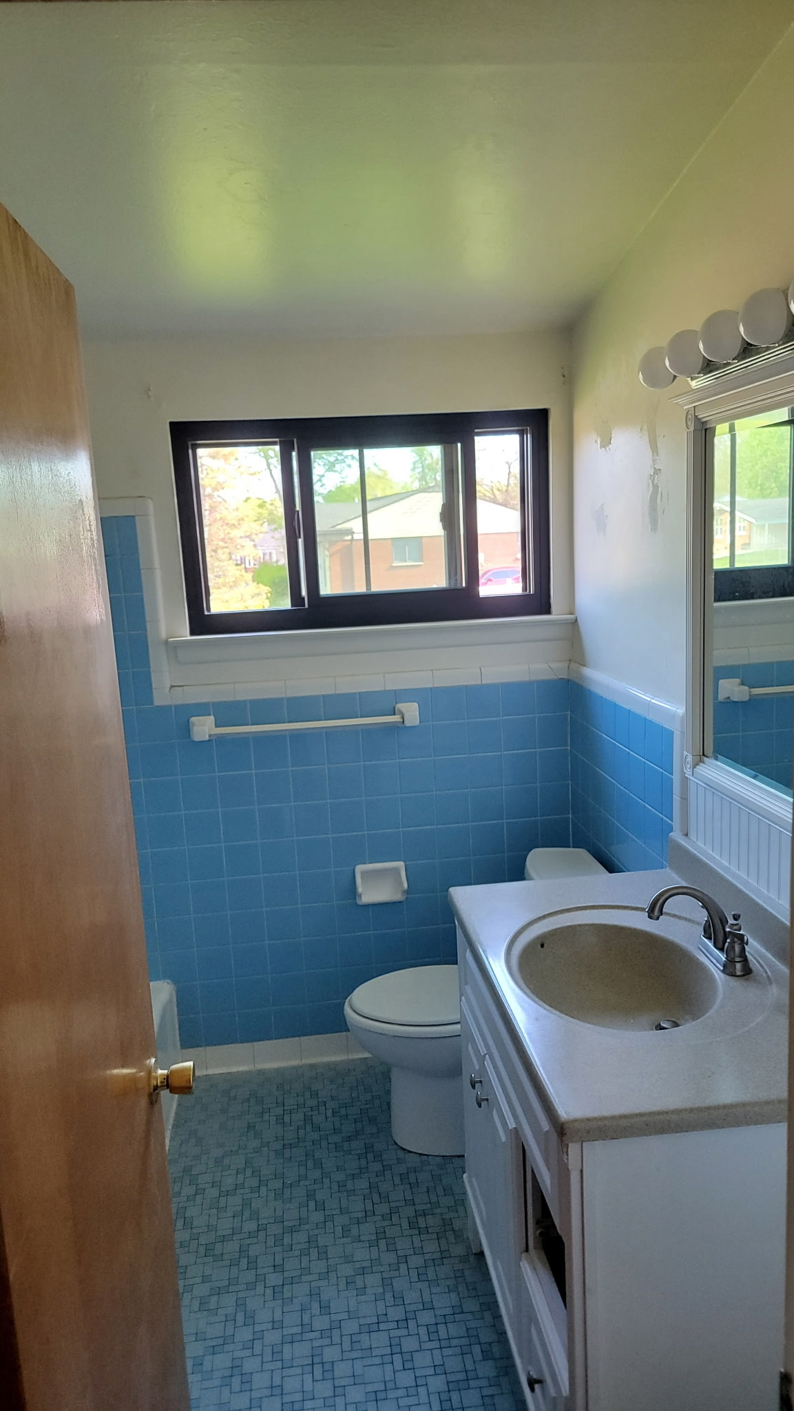 Blue tiled bathroom with white vanity, toilet, and window.