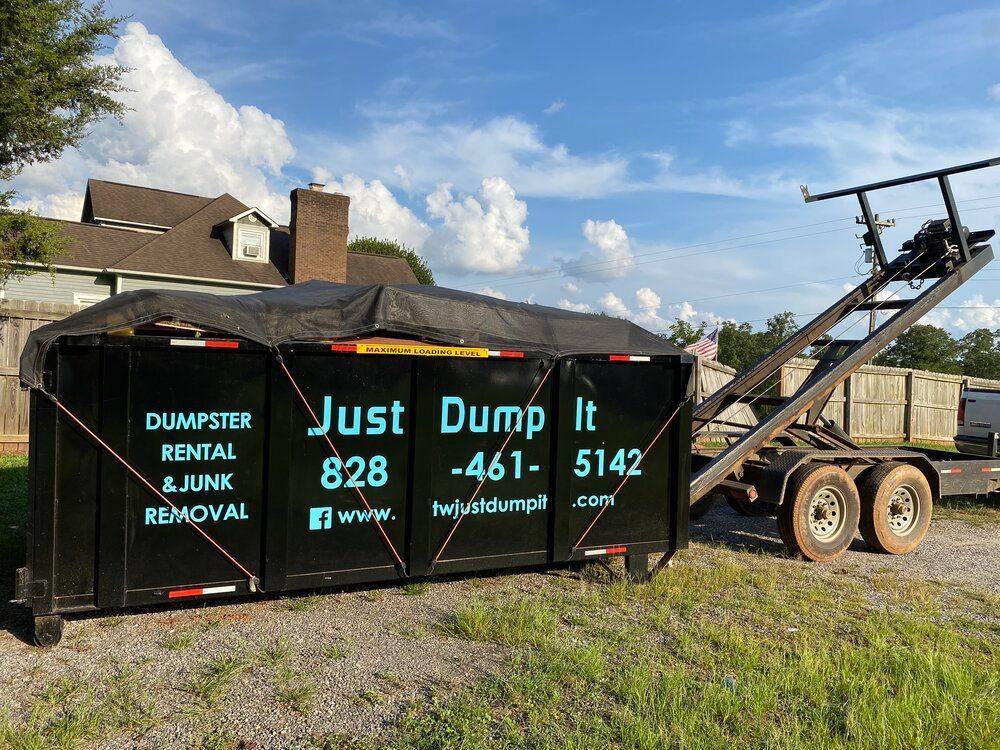 A dumpster is sitting on top of a dirt field next to a trailer.