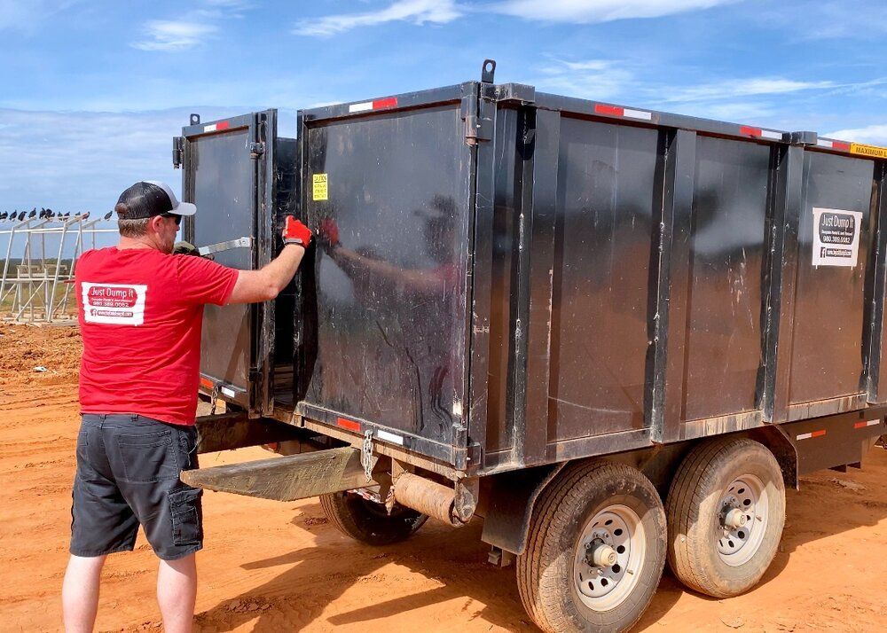 A man in a red shirt is standing next to a dumpster trailer.