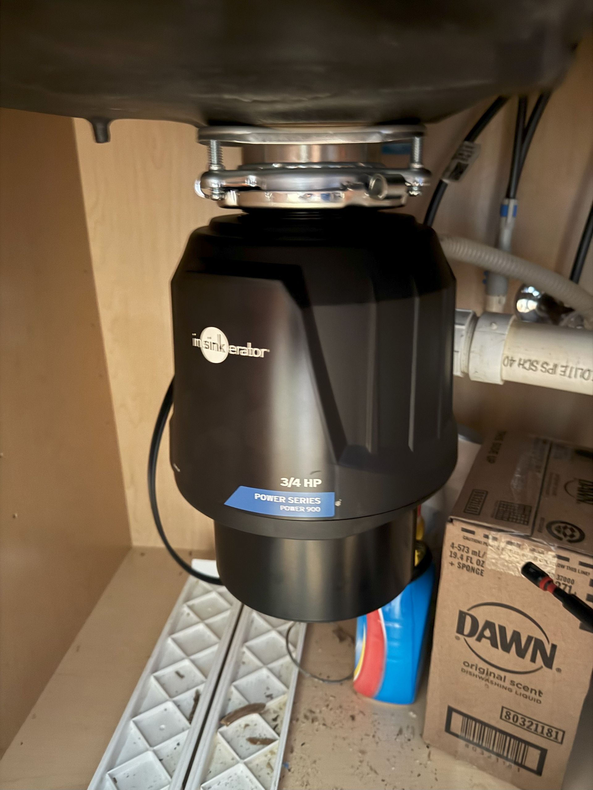 Garbage disposal unit mounted under a kitchen sink. Black with silver accents, various plumbing.