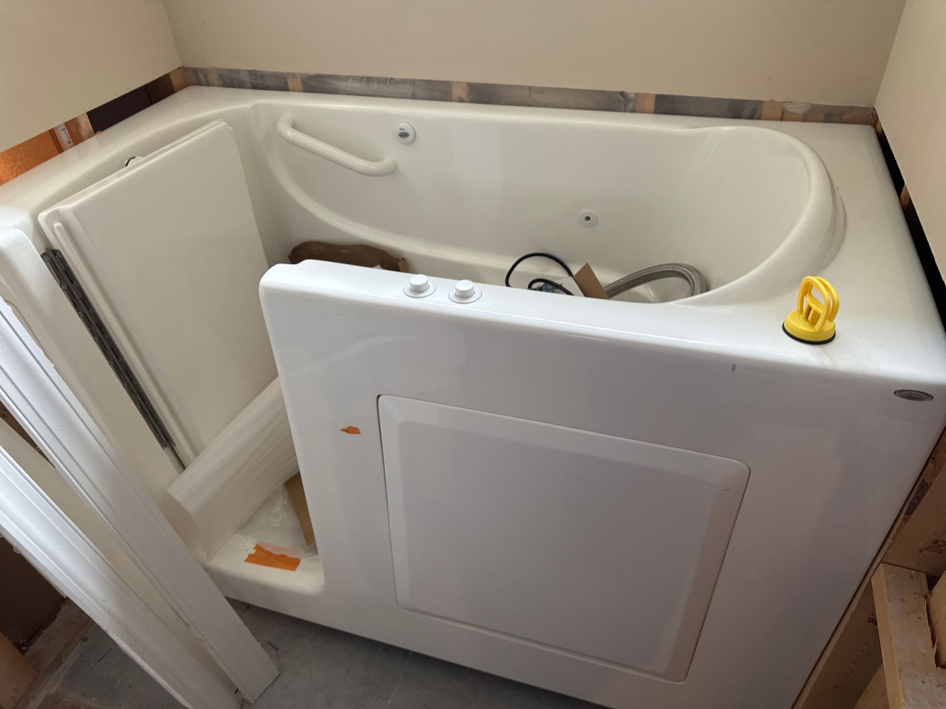 White walk-in bathtub with open door, control panel, and showerhead. Set in a bathroom.