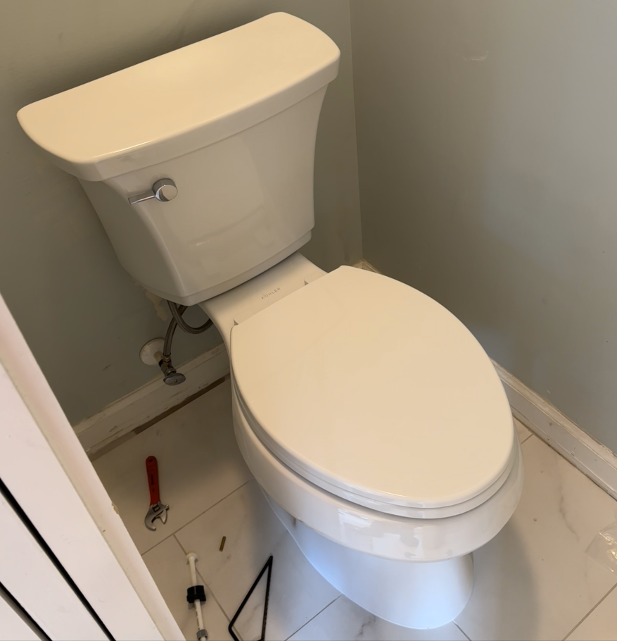 White toilet in a corner of a bathroom with light gray walls and white tile floor.