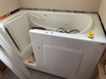 White walk-in bathtub with open door, control panel, and showerhead. Set in a bathroom.