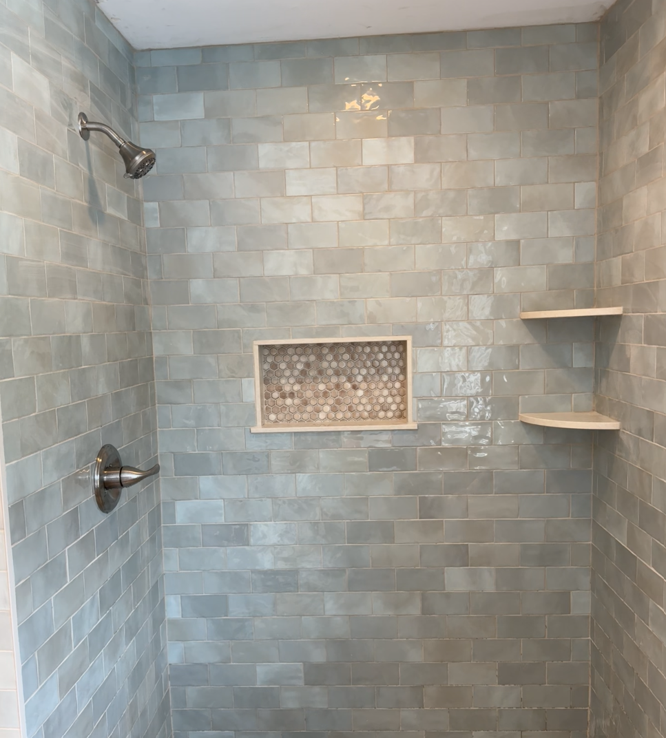 Shower with blue-green rectangular tiles, built-in shelves, and a mosaic-tiled niche.
