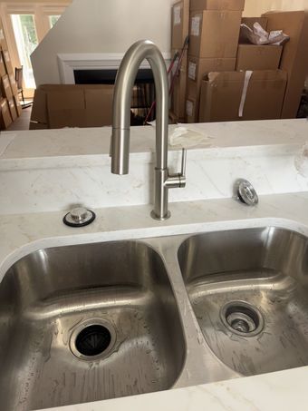 Stainless steel kitchen sink with a pull-down faucet on a white countertop.