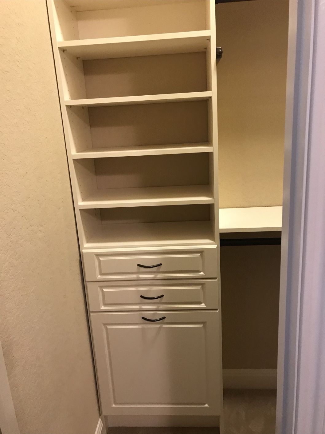 a walk in closet system with shelves , drawers , and a trash can .