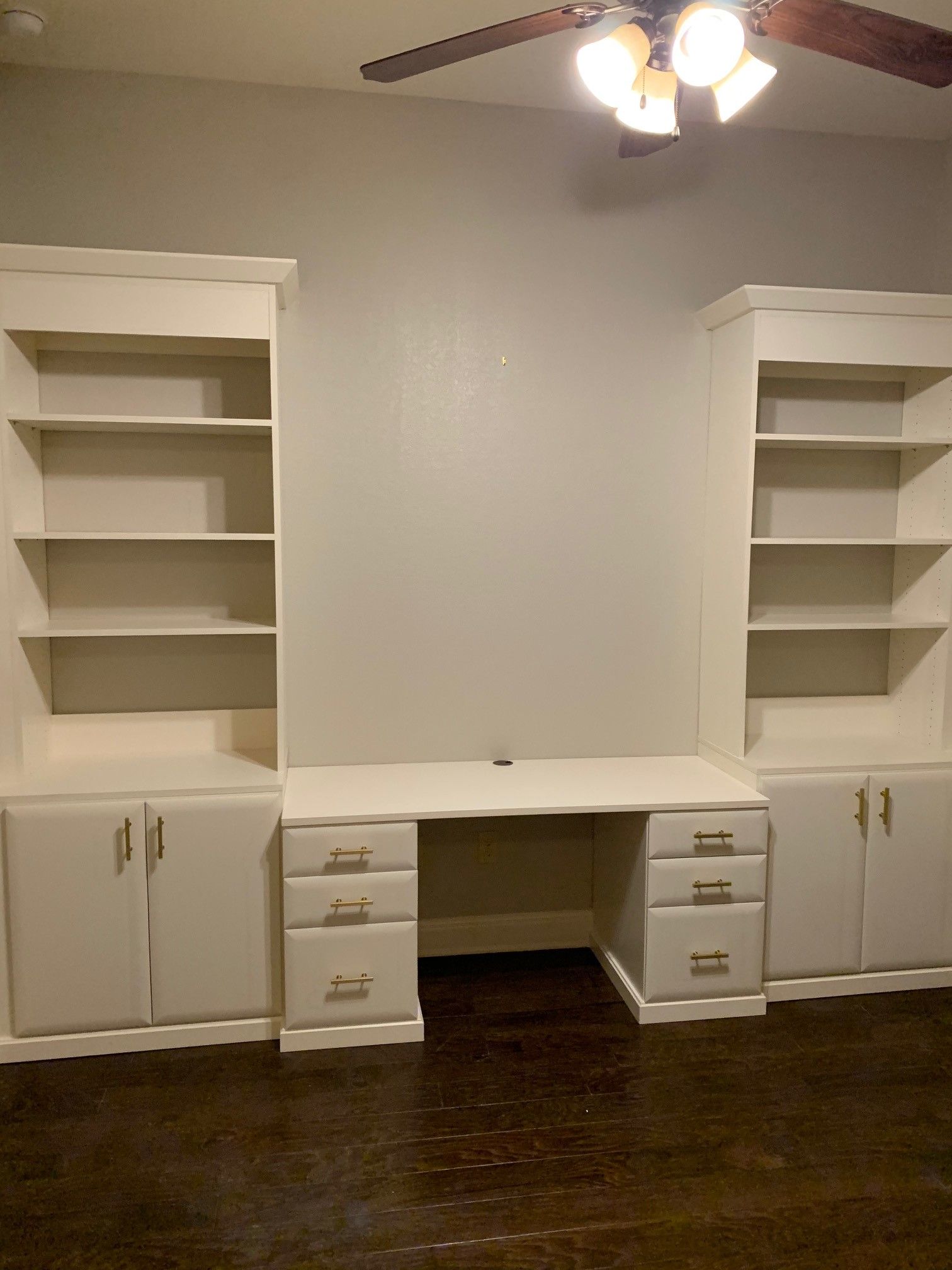 a home office with a desk and shelves and a ceiling fan
