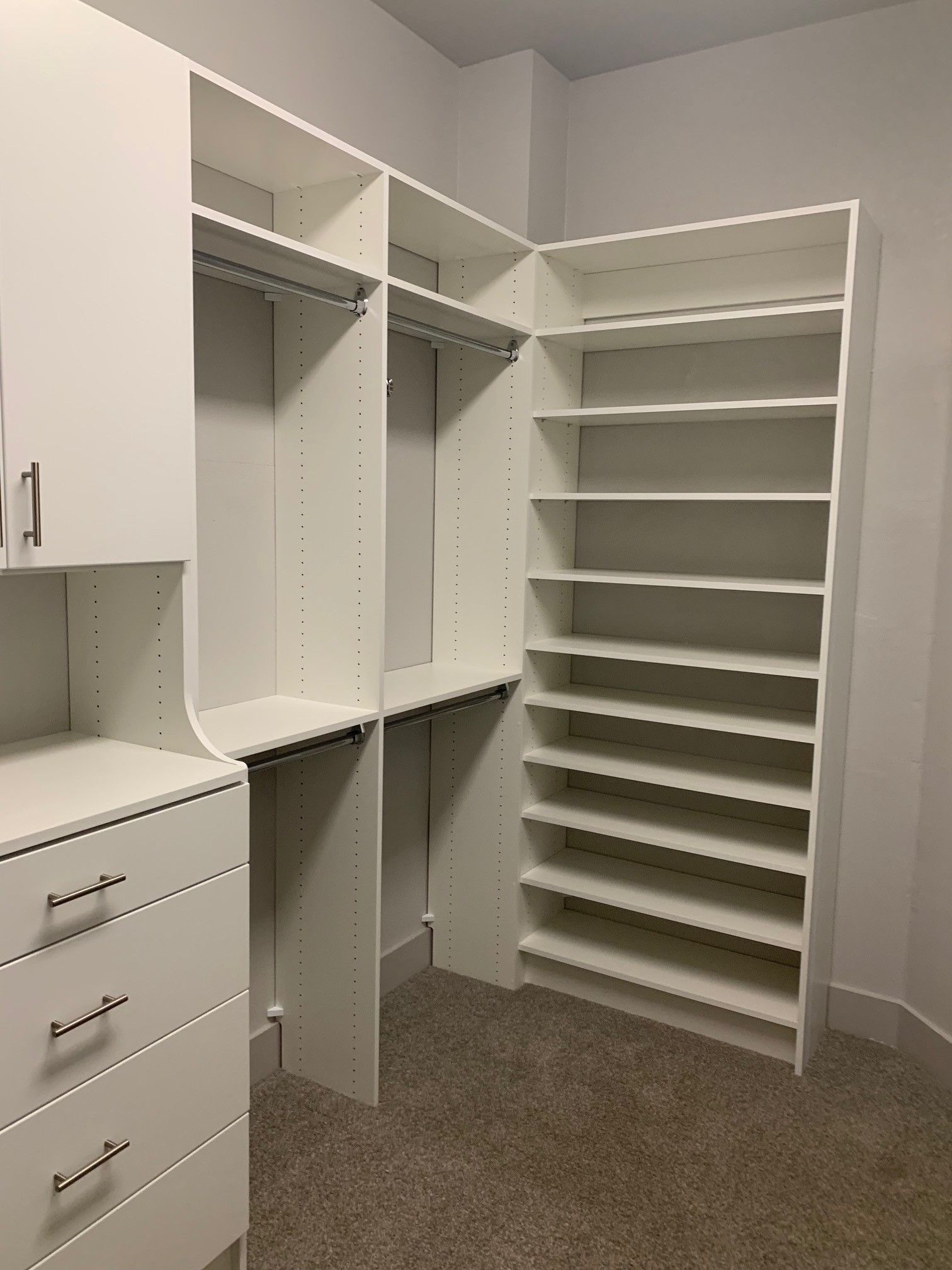 a white walk in closet system with lots of shelves and drawers .