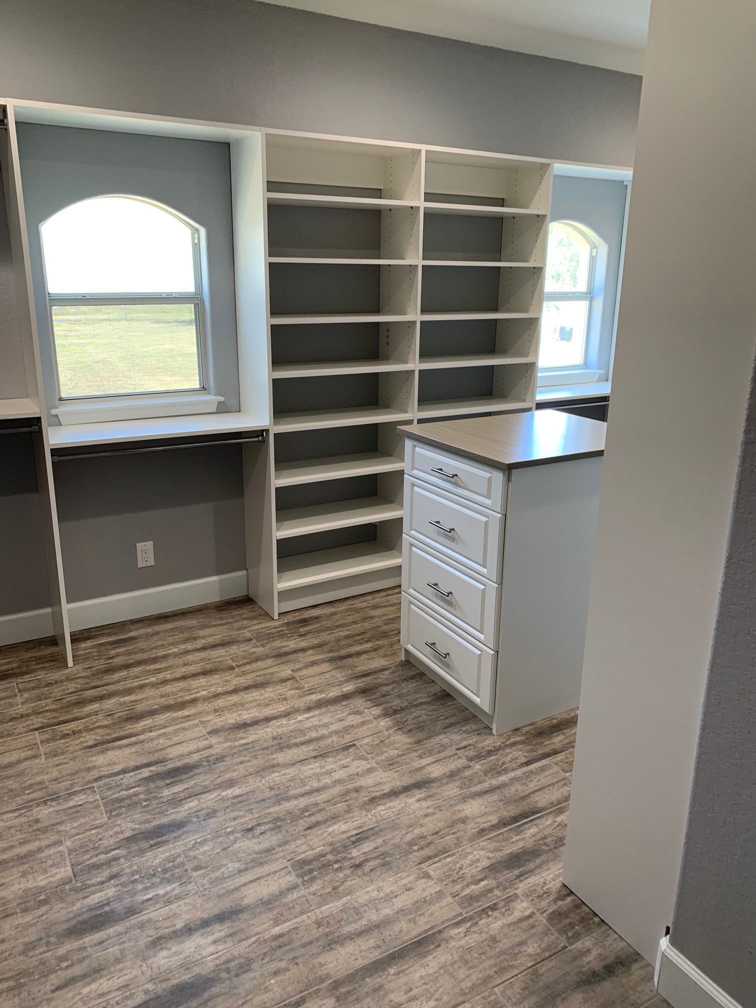a walk in custom closet with lots of shelving and an island .