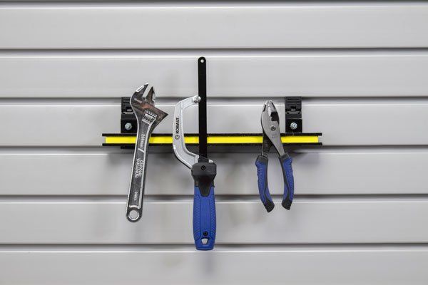 a wrench , pliers , and a screwdriver are hanging on a magnetic tool rack .
