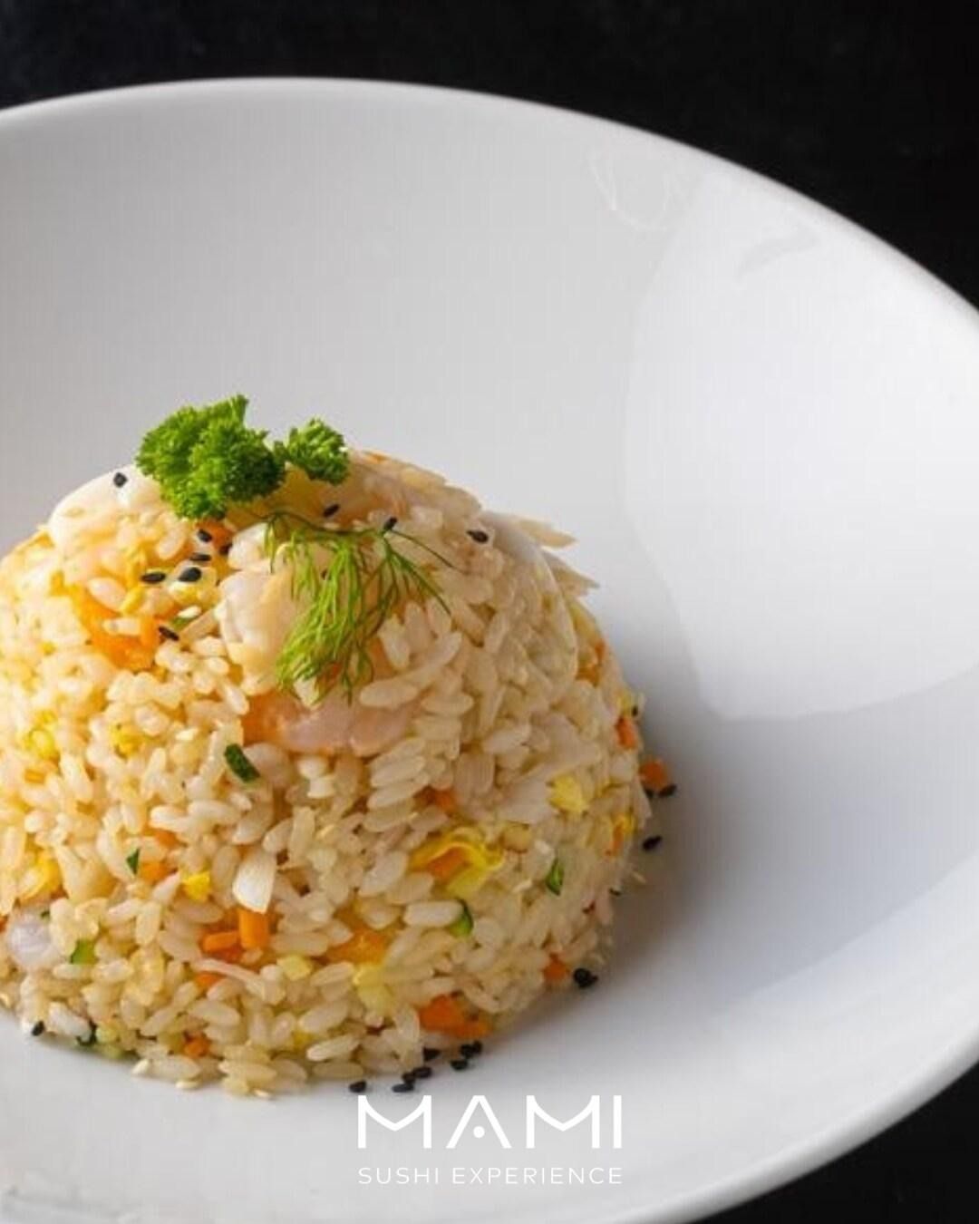 Riso fritto con gamberi e verdure in una ciotola bianca, guarnito con erbe aromatiche e semi di sesamo.