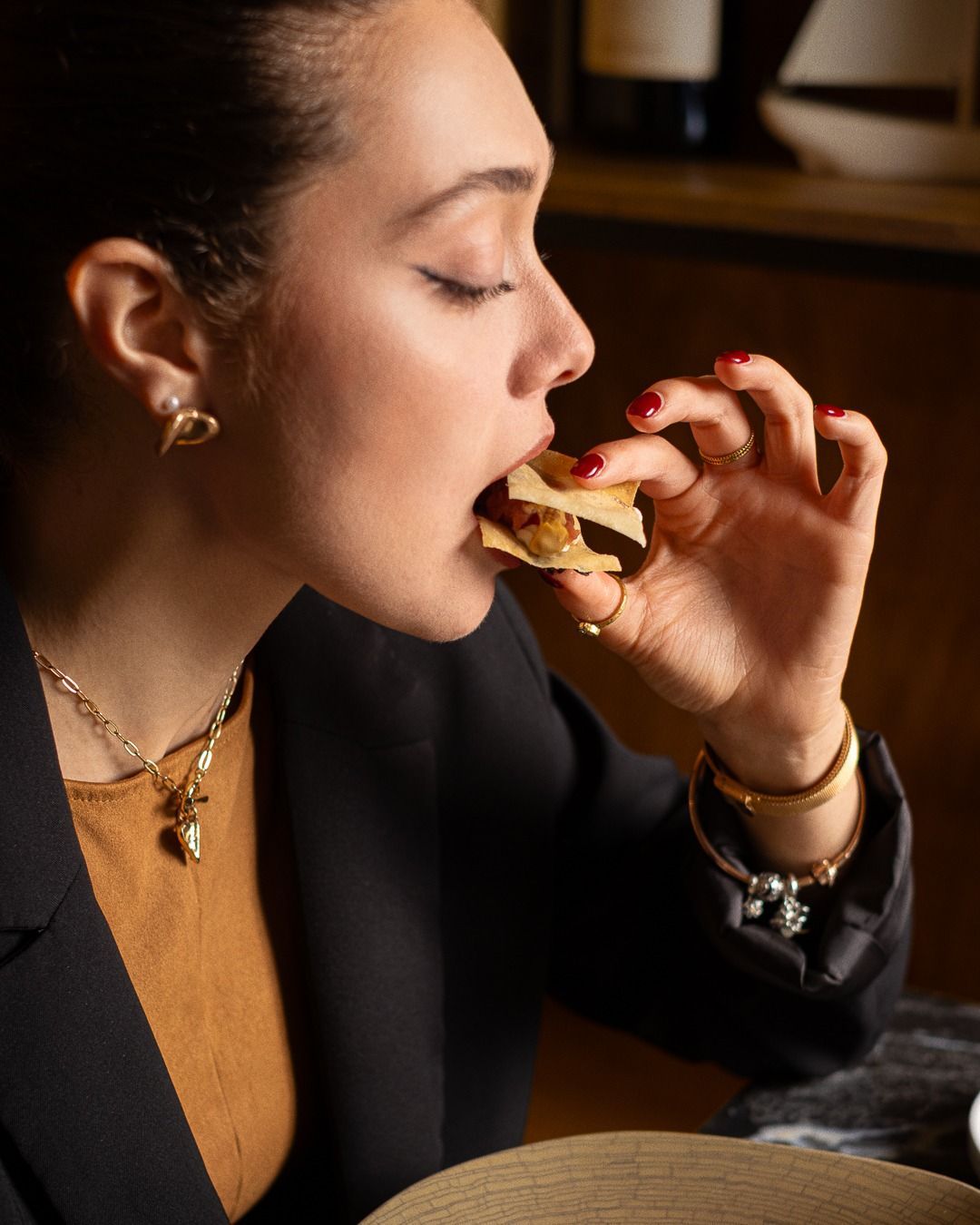 Donna che mangia, indossa gioielli e indossa un blazer nero, primo piano, ambientazione interna.