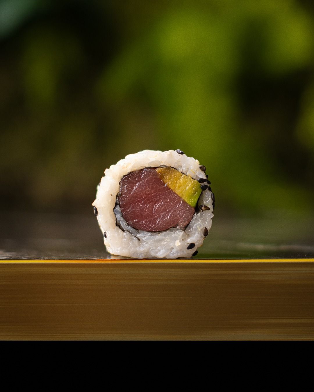Rotolo di sushi con tonno e avocado, su una superficie di bambù e su uno sfondo verde sfocato.