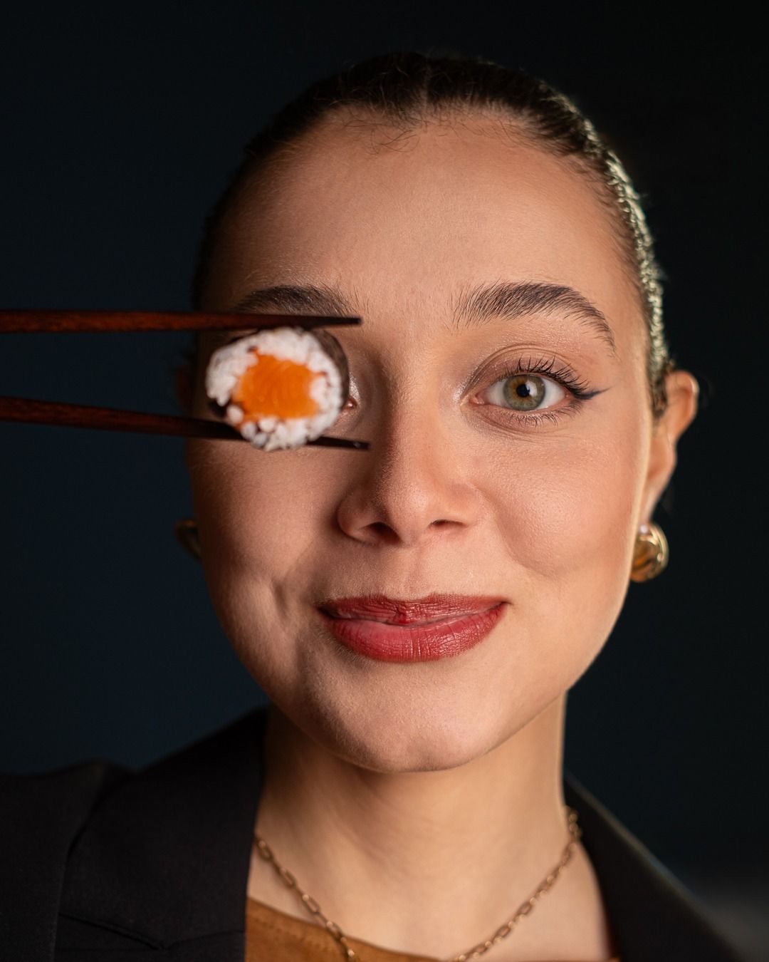 Donna che tiene in mano un rotolo di sushi con le bacchette e guarda la telecamera.