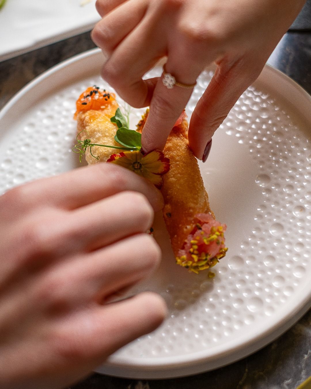 Mani che dispongono i panini fritti su un piatto bianco testurizzato; primo piano.