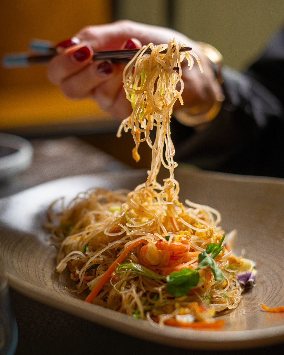 Persona che usa le bacchette per sollevare i noodles da un piatto di frittura.