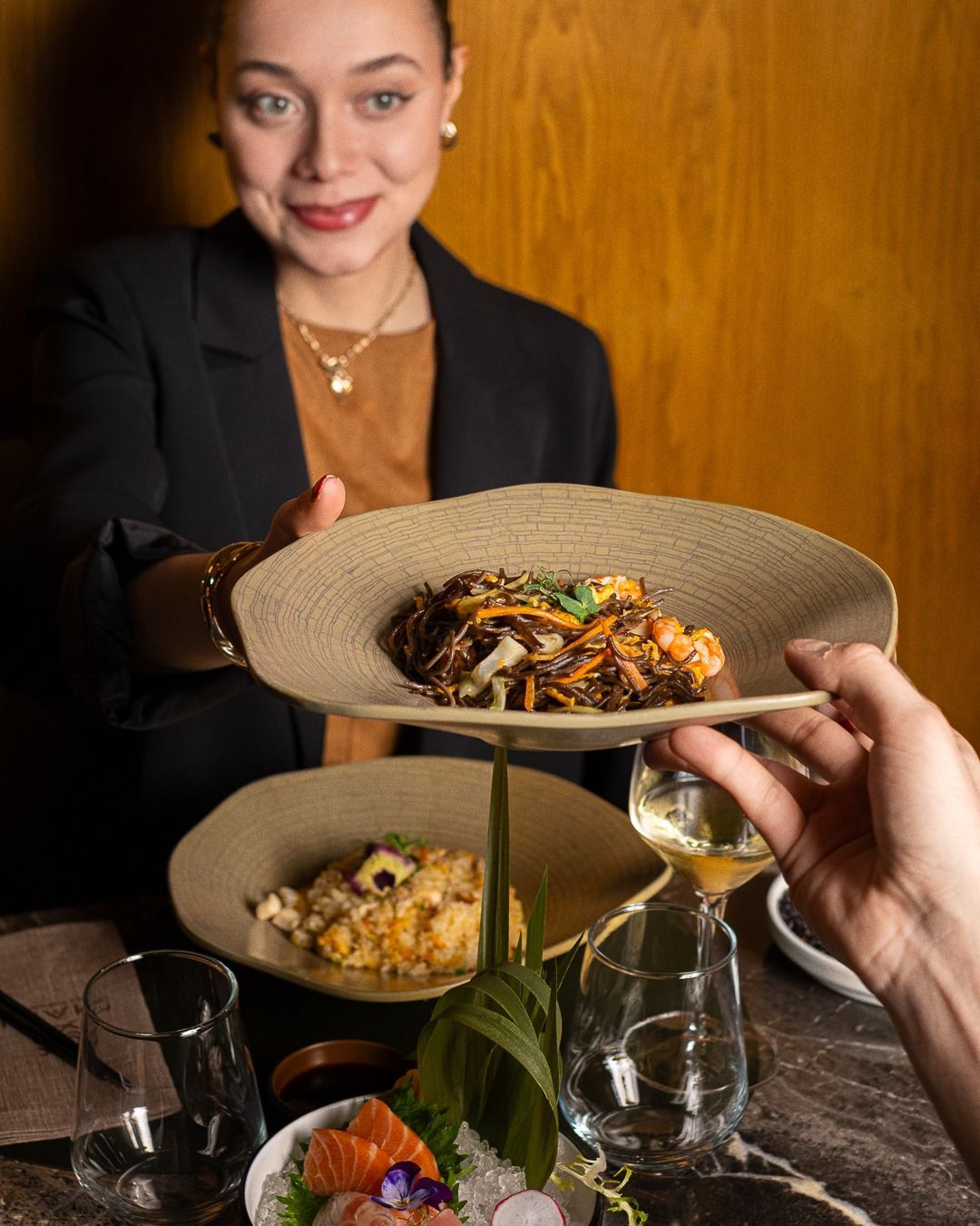 Donna che serve il cibo a un tavolo con piatti e un bicchiere di vino.