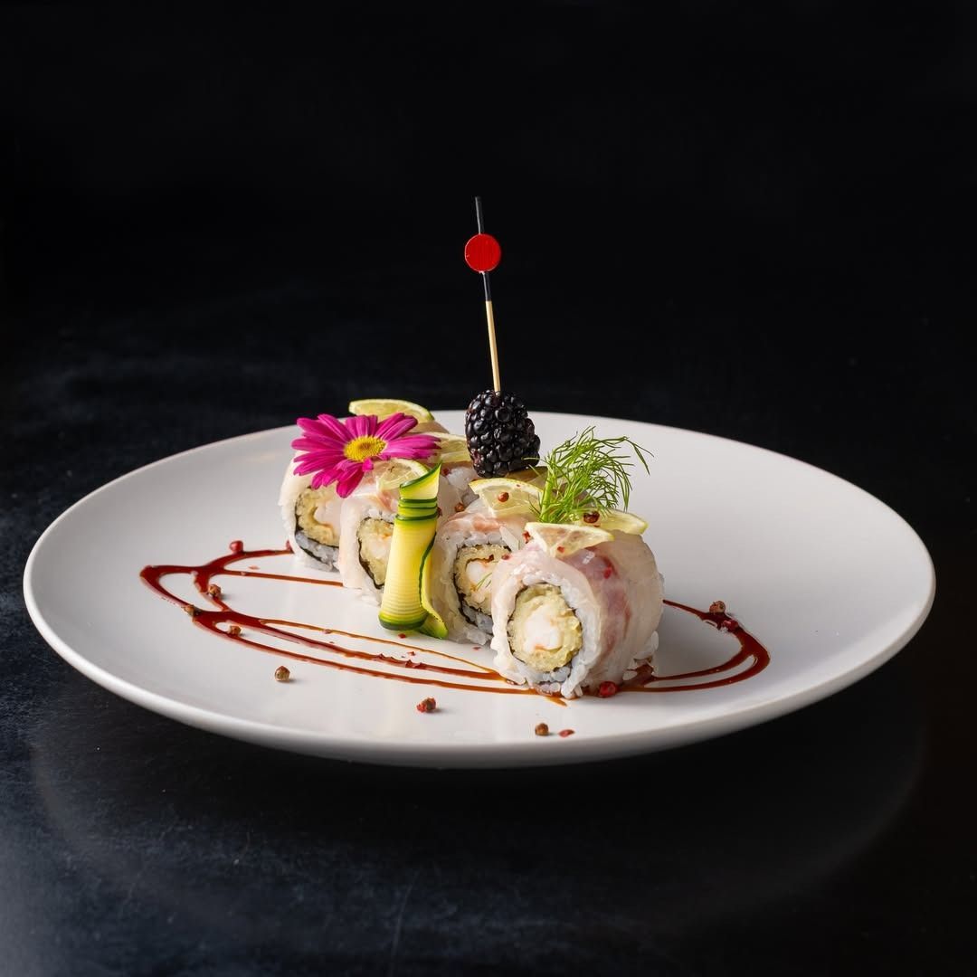 Rotolo di sushi con guarnizione decorativa su un piatto bianco, sfondo scuro.