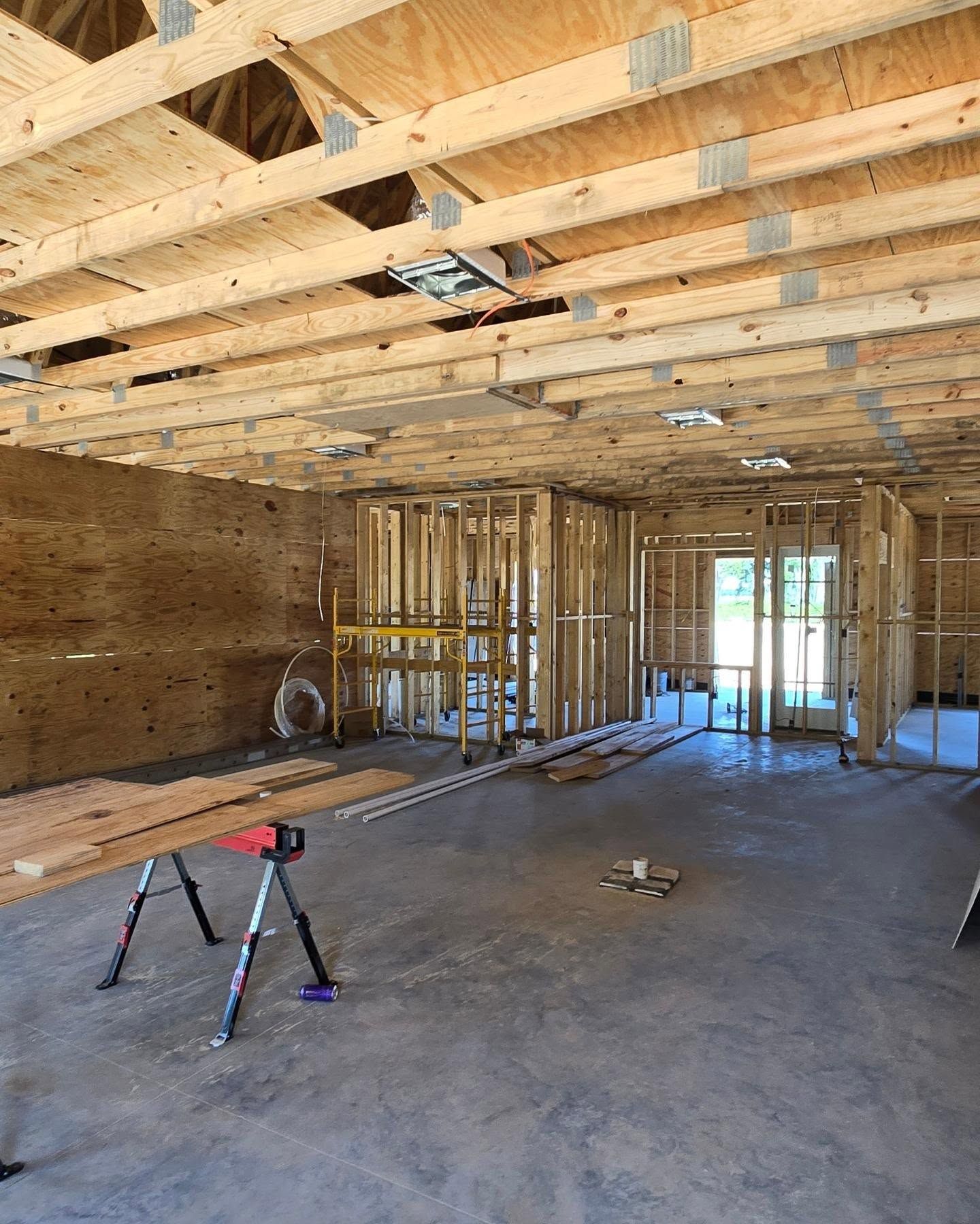 Interior view of a building under construction, showing wooden framing, exposed beams, and concrete floor.