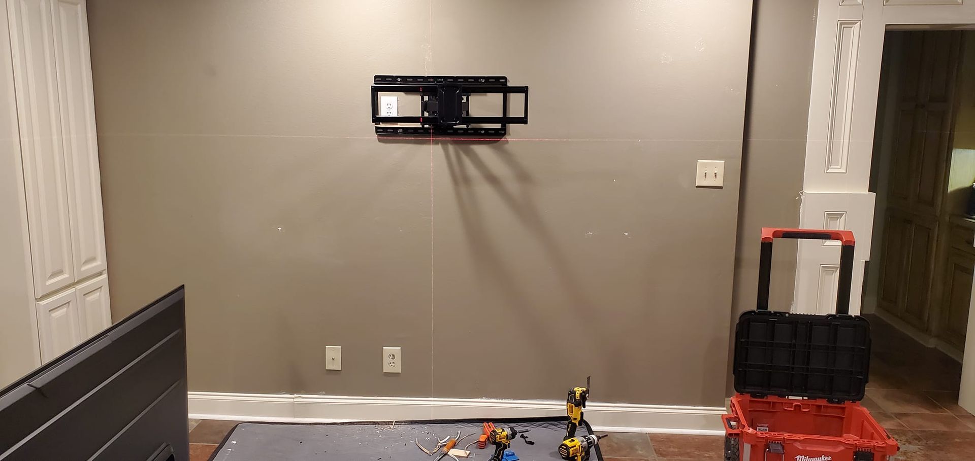A wall-mounted TV bracket above a low ground with tools and a toolbox.