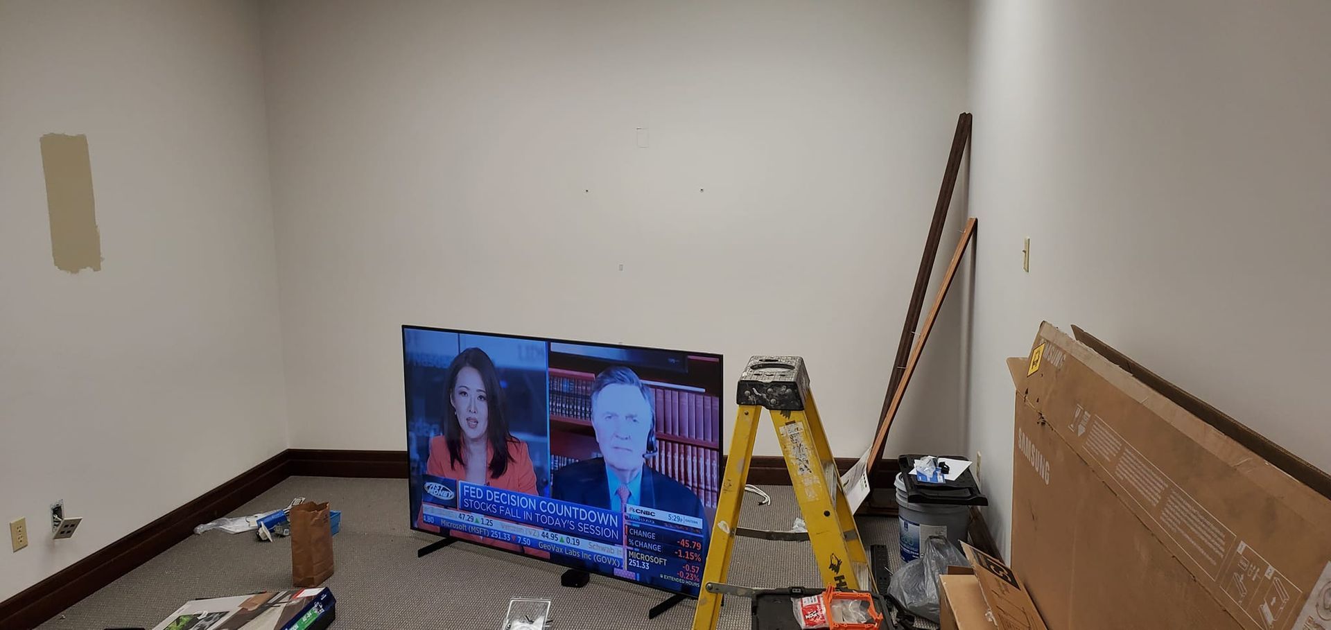 Room with TV on floor, ladder, and construction materials. Walls are white with brown baseboards.