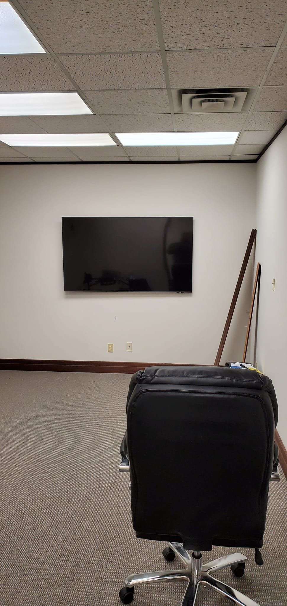 A black office chair in an empty room, a TV on the wall, and the carpet has a swirling pattern.